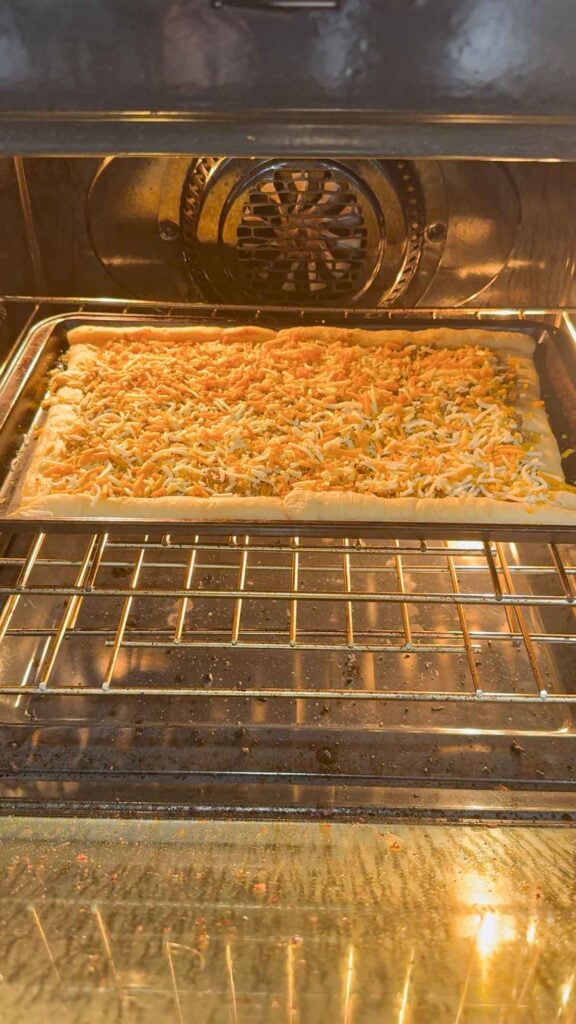 taco pizza topped with shredded nacho cheese baking in the oven