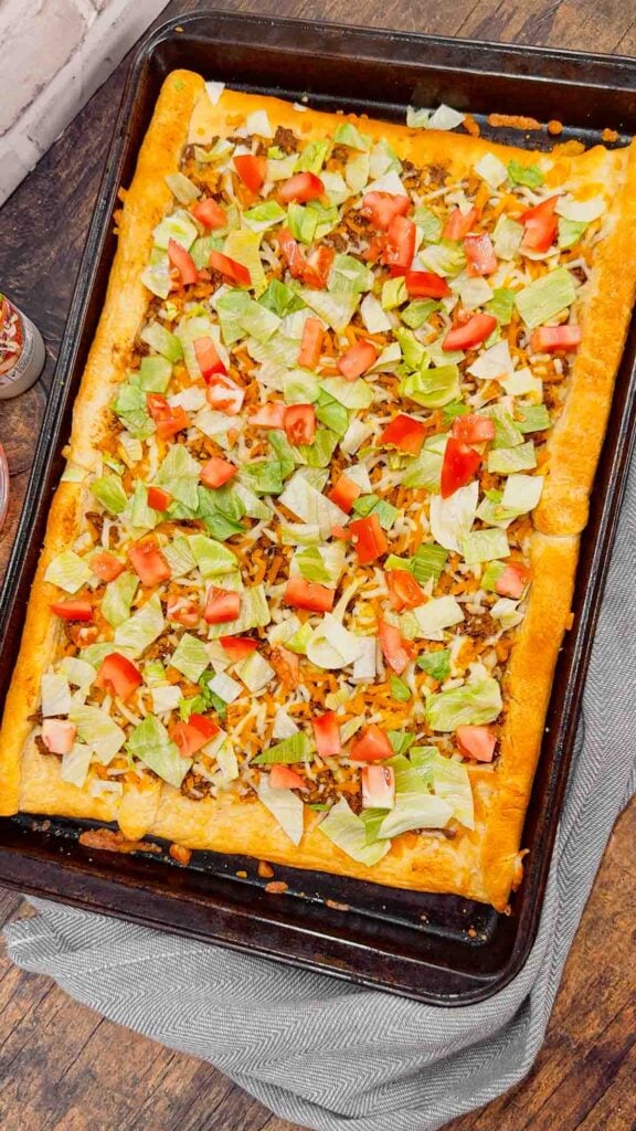 Taco Pizza with Crescent Rolls is a family friendly ground beef dinner recipe perfect for busy weeknights. This tasty pizza starts of with a Pillsbury crescent roll crust and is topped with a ground beef and cream cheese taco mixture, shredded nacho cheese, lettuce, tomatoes and mini Doritos nacho chips.