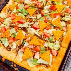 Taco Pizza with Crescent Rolls is a family friendly ground beef dinner recipe perfect for busy weeknights. This tasty pizza starts of with a Pillsbury crescent roll crust and is topped with a ground beef and cream cheese taco mixture, shredded nacho cheese, lettuce, tomatoes and mini Doritos nacho chips.