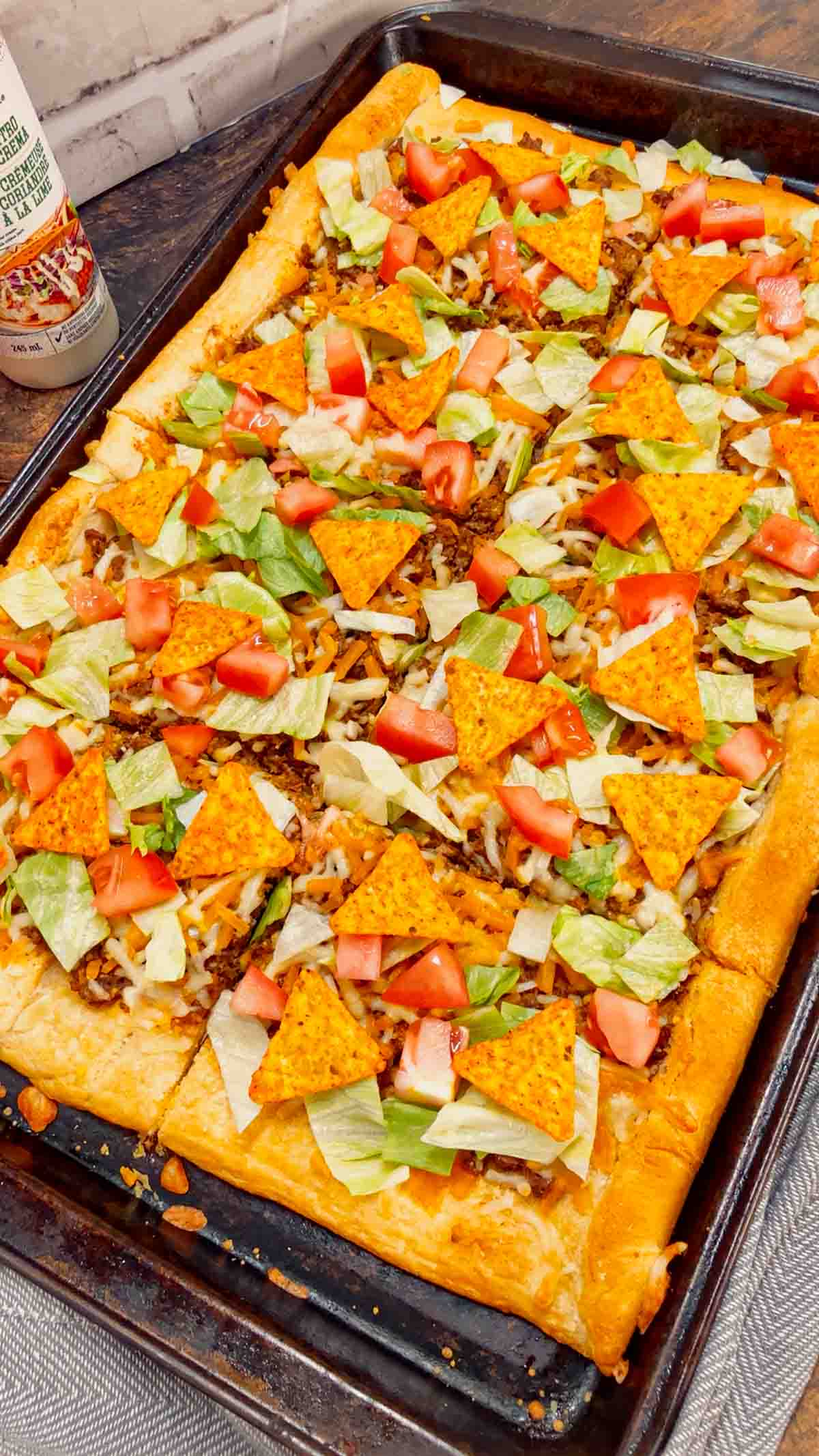Taco Pizza with Crescent Rolls is a family friendly ground beef dinner recipe perfect for busy weeknights. This tasty pizza starts of with a Pillsbury crescent roll crust and is topped with a ground beef and cream cheese taco mixture, shredded nacho cheese, lettuce, tomatoes and mini Doritos nacho chips.