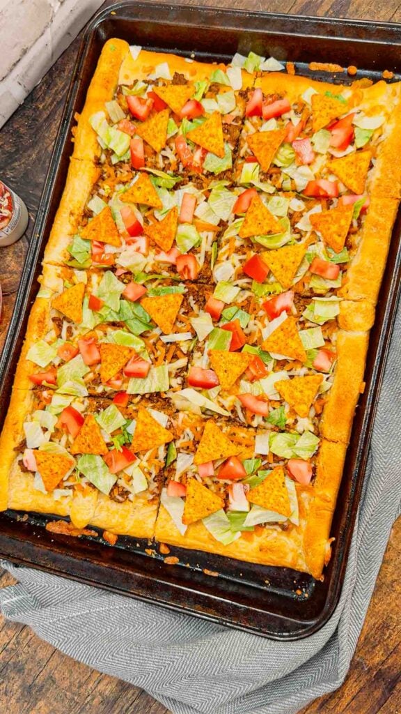 Taco Pizza with Crescent Rolls is a family friendly ground beef dinner recipe perfect for busy weeknights. This tasty pizza starts of with a Pillsbury crescent roll crust and is topped with a ground beef and cream cheese taco mixture, shredded nacho cheese, lettuce, tomatoes and mini Doritos nacho chips.