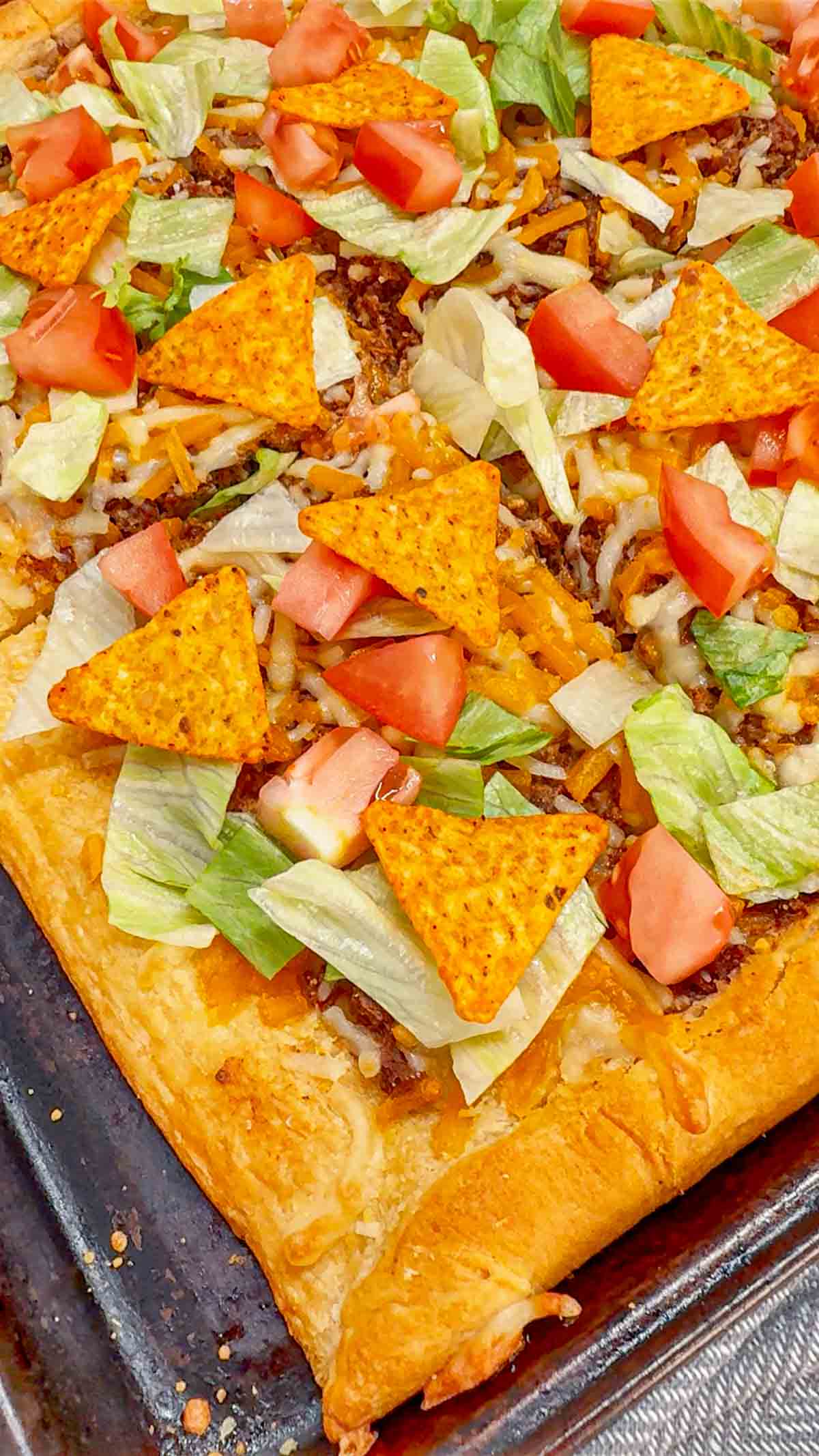 Taco Pizza with Crescent Rolls is a family friendly ground beef dinner recipe perfect for busy weeknights. This tasty pizza starts of with a Pillsbury crescent roll crust and is topped with a ground beef and cream cheese taco mixture, shredded nacho cheese, lettuce, tomatoes and mini Doritos nacho chips.