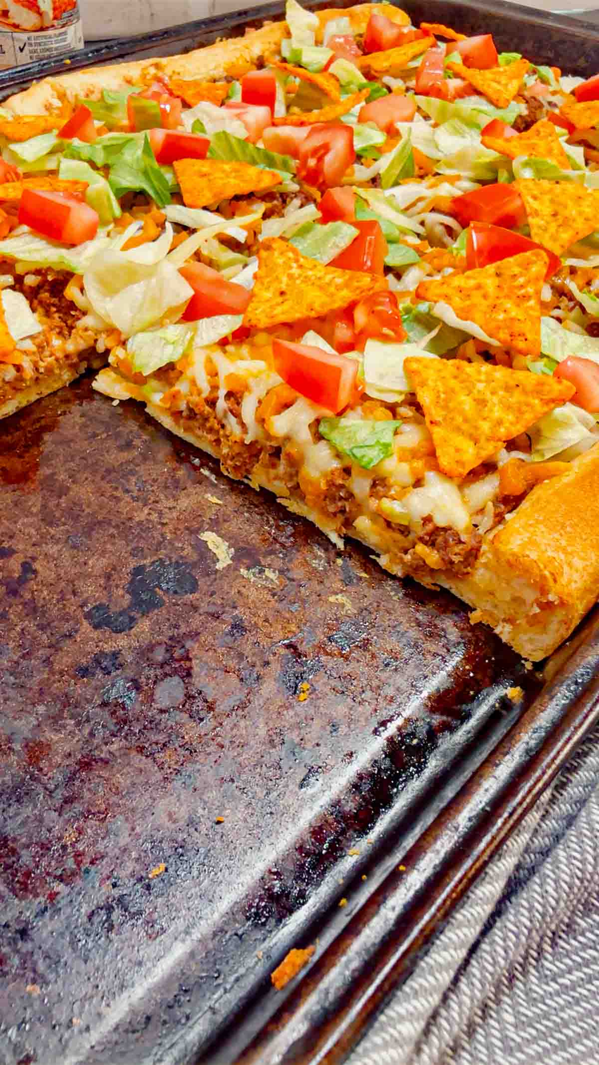 Taco Pizza with Crescent Rolls is a family friendly ground beef dinner recipe perfect for busy weeknights. This tasty pizza starts of with a Pillsbury crescent roll crust and is topped with a ground beef and cream cheese taco mixture, shredded nacho cheese, lettuce, tomatoes and mini Doritos nacho chips.