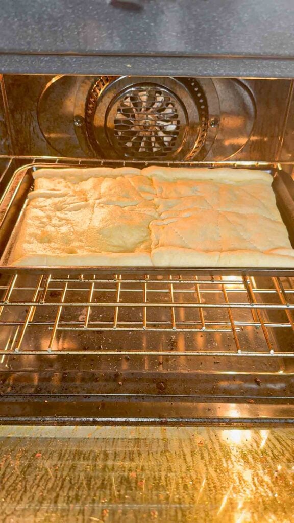 crescent roll dough baking on a cookie sheet in the oven