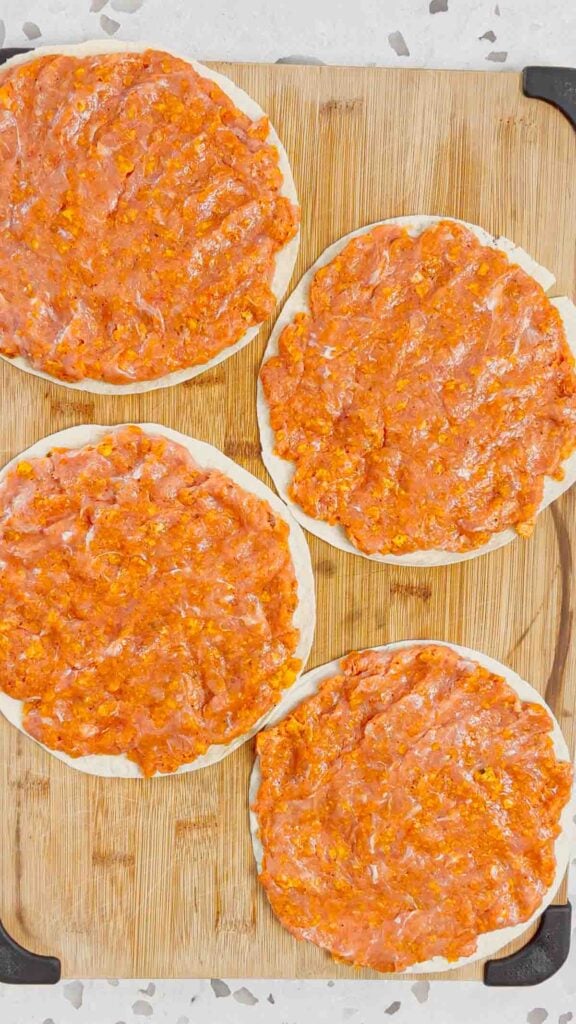 raw ground chicken and crushed doritos mixture spread on flour tortillas