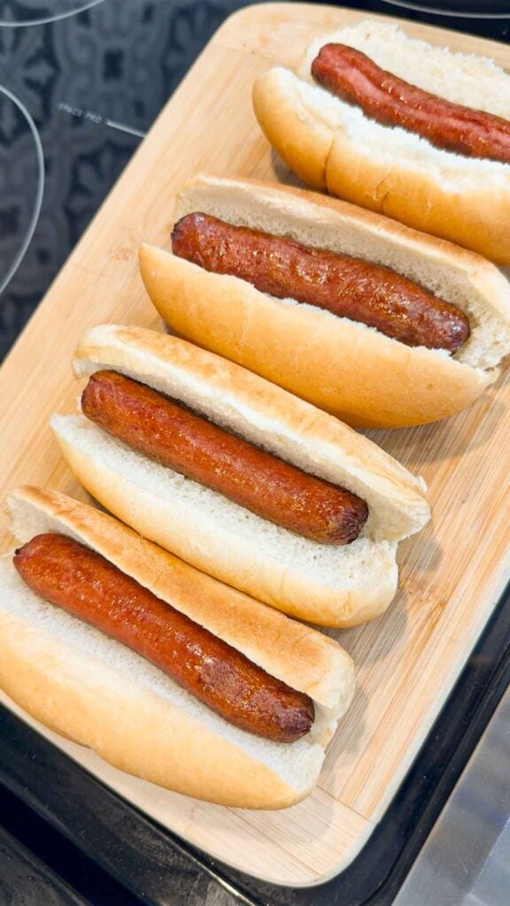 cooked wieners added to buns on a cutting board
