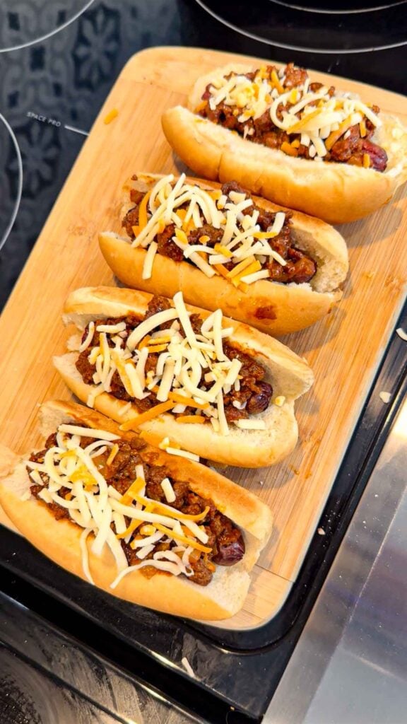 shredded cheese on top of sloppy joe dogs on a cutting board