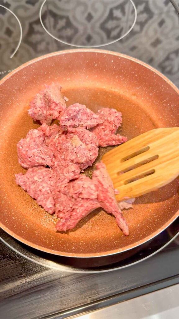 raw ground beef being broken apart in a skillet