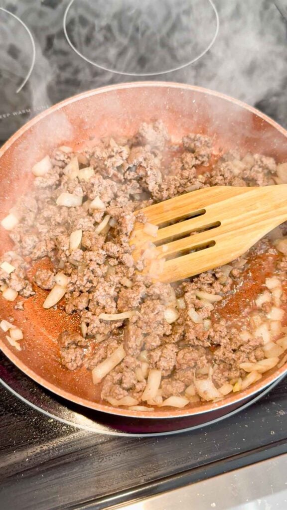 ground beef and diced onions cooking in a skillet