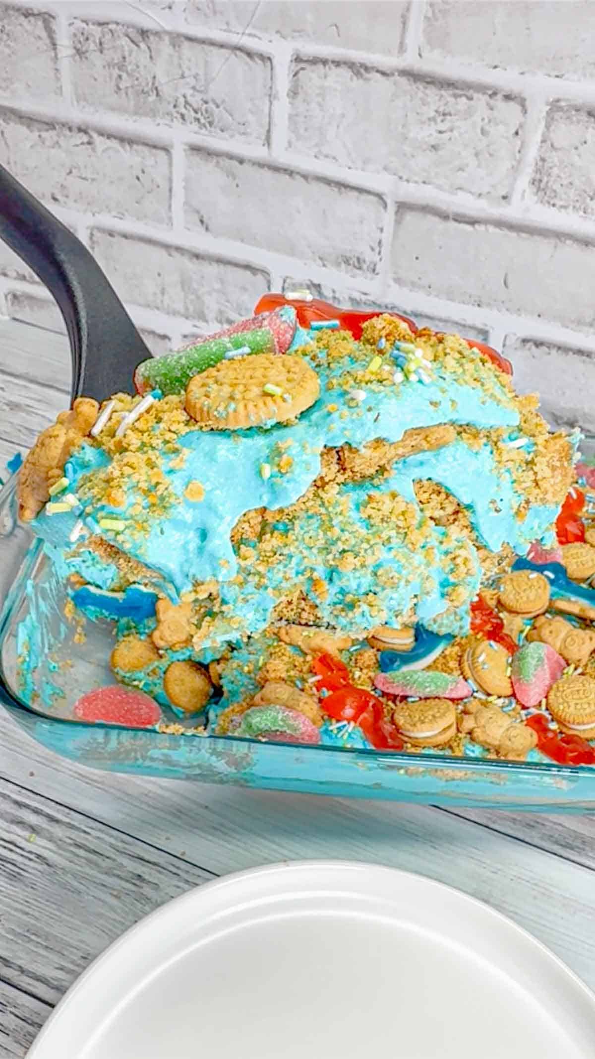 Summer Dirt Cake is an easy no bake dessert recipe perfect for parties and potlucks. This beach themed dirt cake is made with golden Oreo and graham cracker crumbs, layered with a delicious cream cheese and vanilla pudding mixture and all topped with mini cookies and beach themed gummy candies.