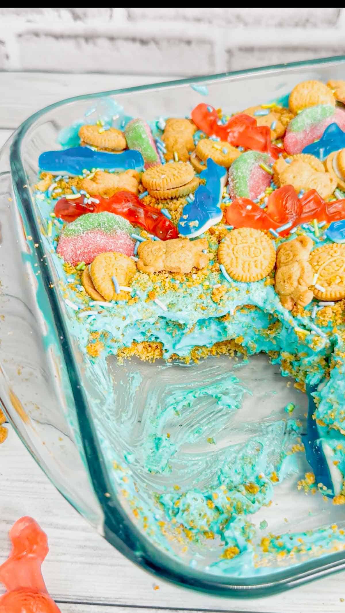 Summer Dirt Cake is an easy no bake dessert recipe perfect for parties and potlucks. This beach themed dirt cake is made with golden Oreo and graham cracker crumbs, layered with a delicious cream cheese and vanilla pudding mixture and all topped with mini cookies and beach themed gummy candies.