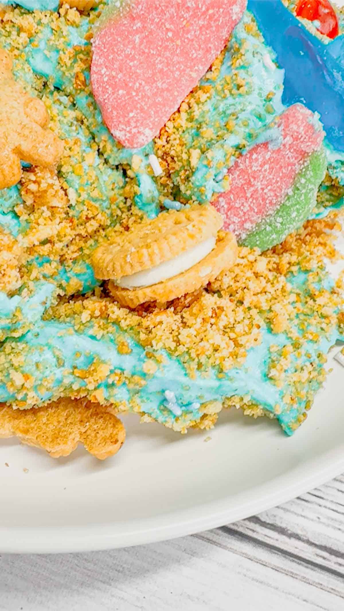 Summer Dirt Cake is an easy no bake dessert recipe perfect for parties and potlucks. This beach themed dirt cake is made with golden Oreo and graham cracker crumbs, layered with a delicious cream cheese and vanilla pudding mixture and all topped with mini cookies and beach themed gummy candies.