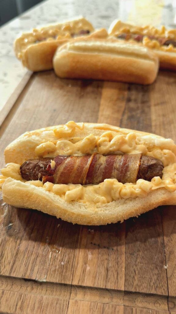 bacon wrapped wiener pushed into mac and cheese on a hot dog bun
