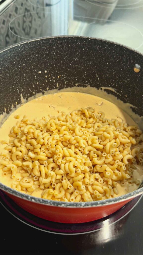 cooked macaroni noodles added to a pot with a creamy cheese sauce