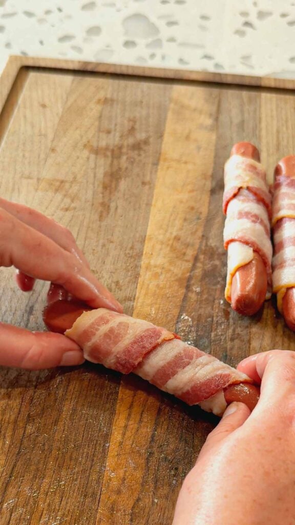 wrapping wieners with bacon on a cutting board