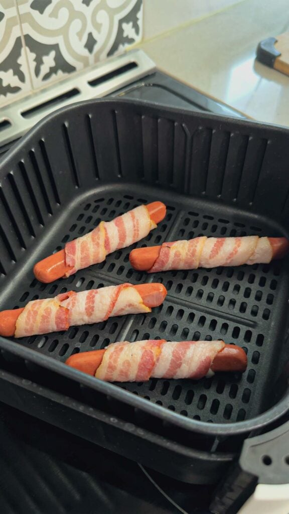uncooked bacon wrapped wieners in an air fryer basket