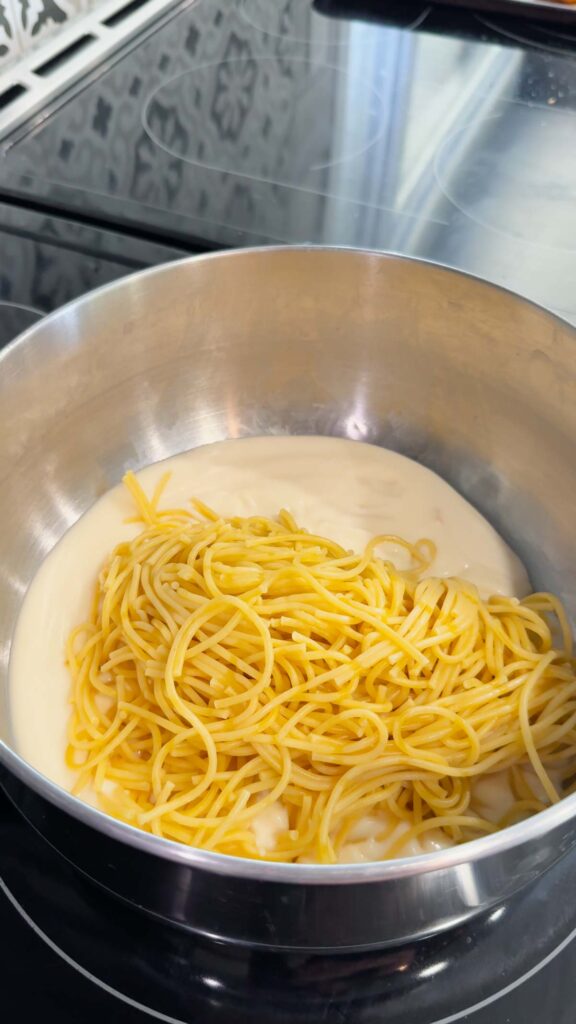 cooked spaghetti added to pot with alfredo sauce