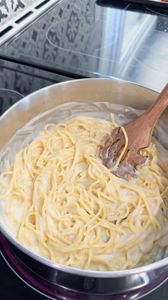 stirring spaghetti noodles and creamy alfredo sauce in a large pot