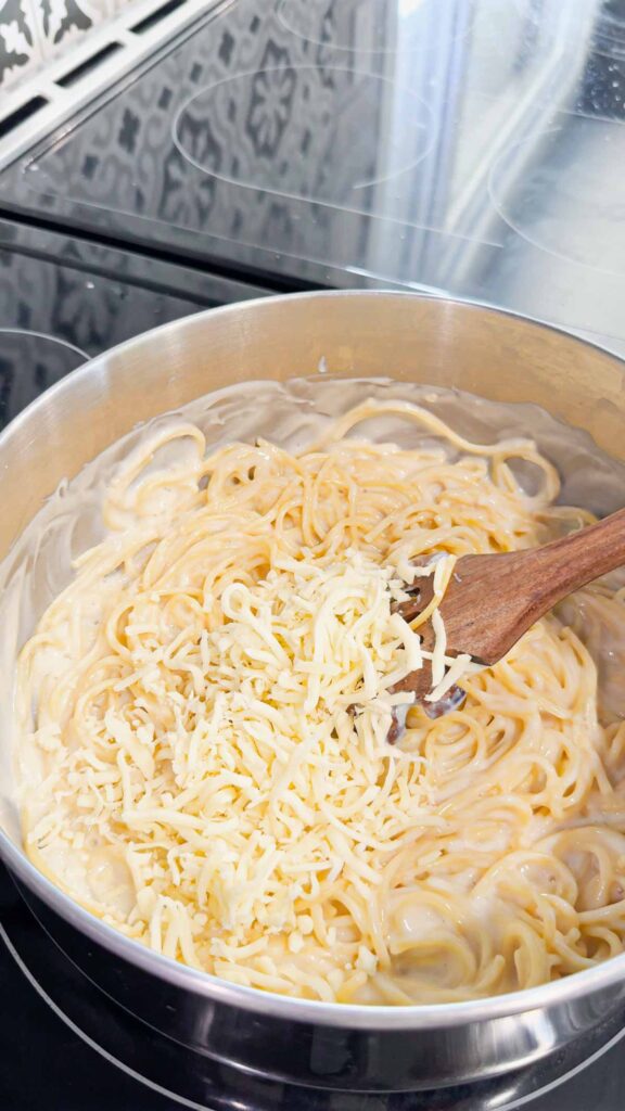 shredded mozzarella cheese added to pot with alfredo spaghetti