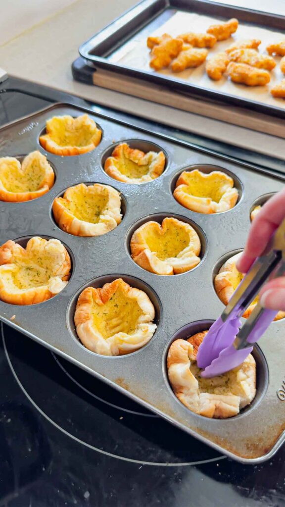 using tongs to press down in center of hamburger bun cups in a muffin tin