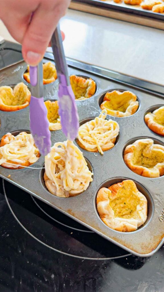 alfredo spaghetti being stuffed into hamburger bun cups in a muffin tin