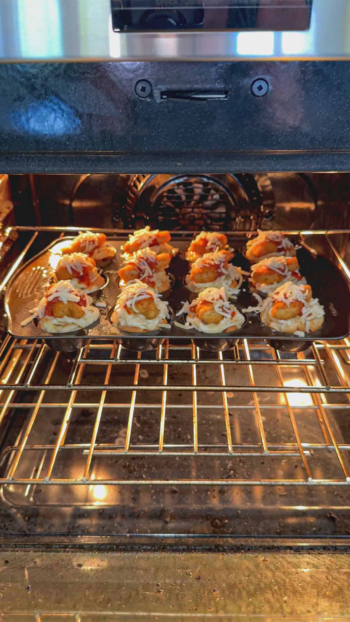 dino nugget chicken parm cups in a muffin tin baking in the oven