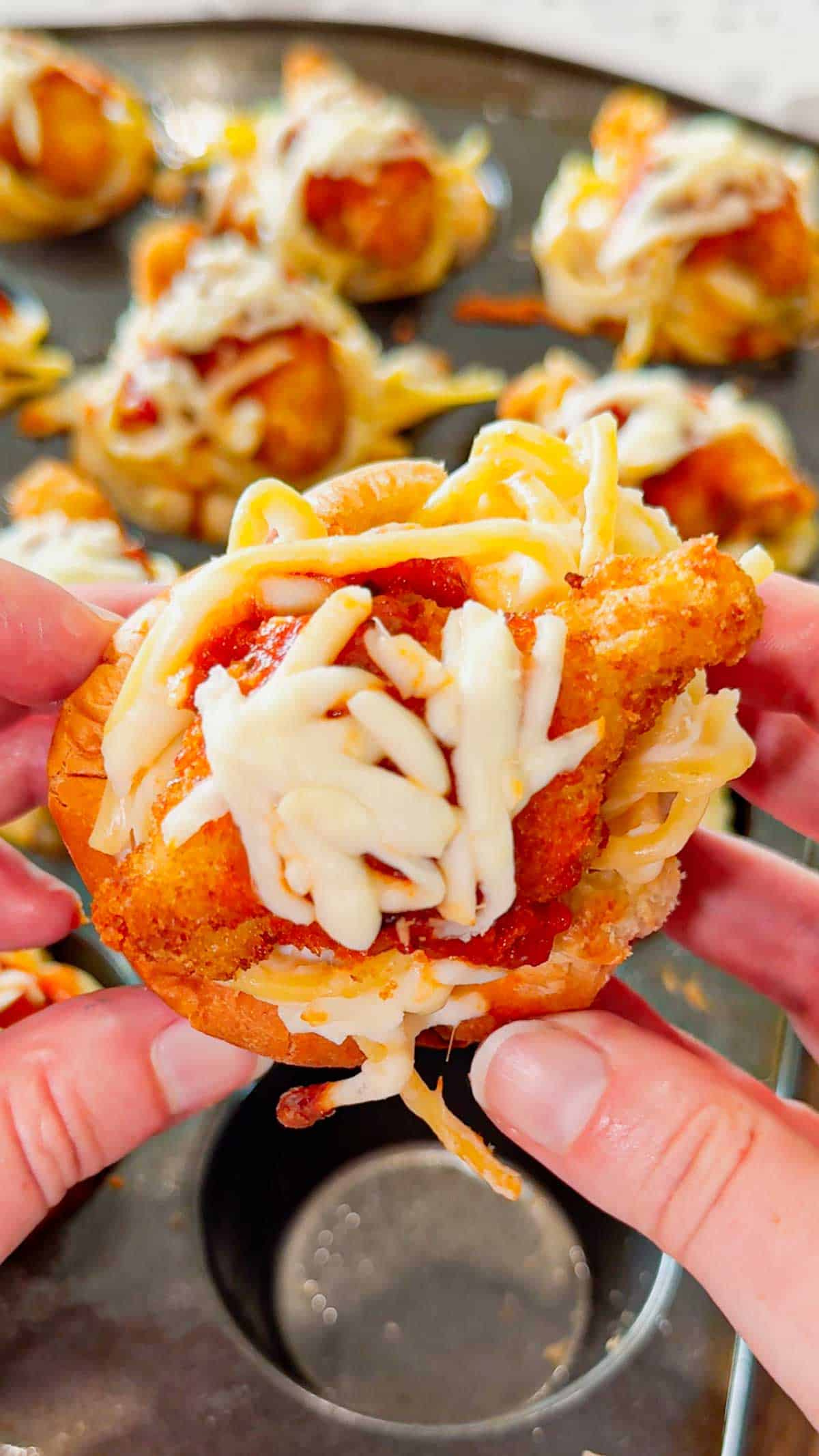 Dino Nugget Chicken Parm Cups are a fun and easy muffin tin dinner the whole family will love. Hamburger buns are spread with garlic butter, baked in muffin tins and stuffed with creamy alfredo spaghetti and topped with dino nuggets, marinara and mozzarella.