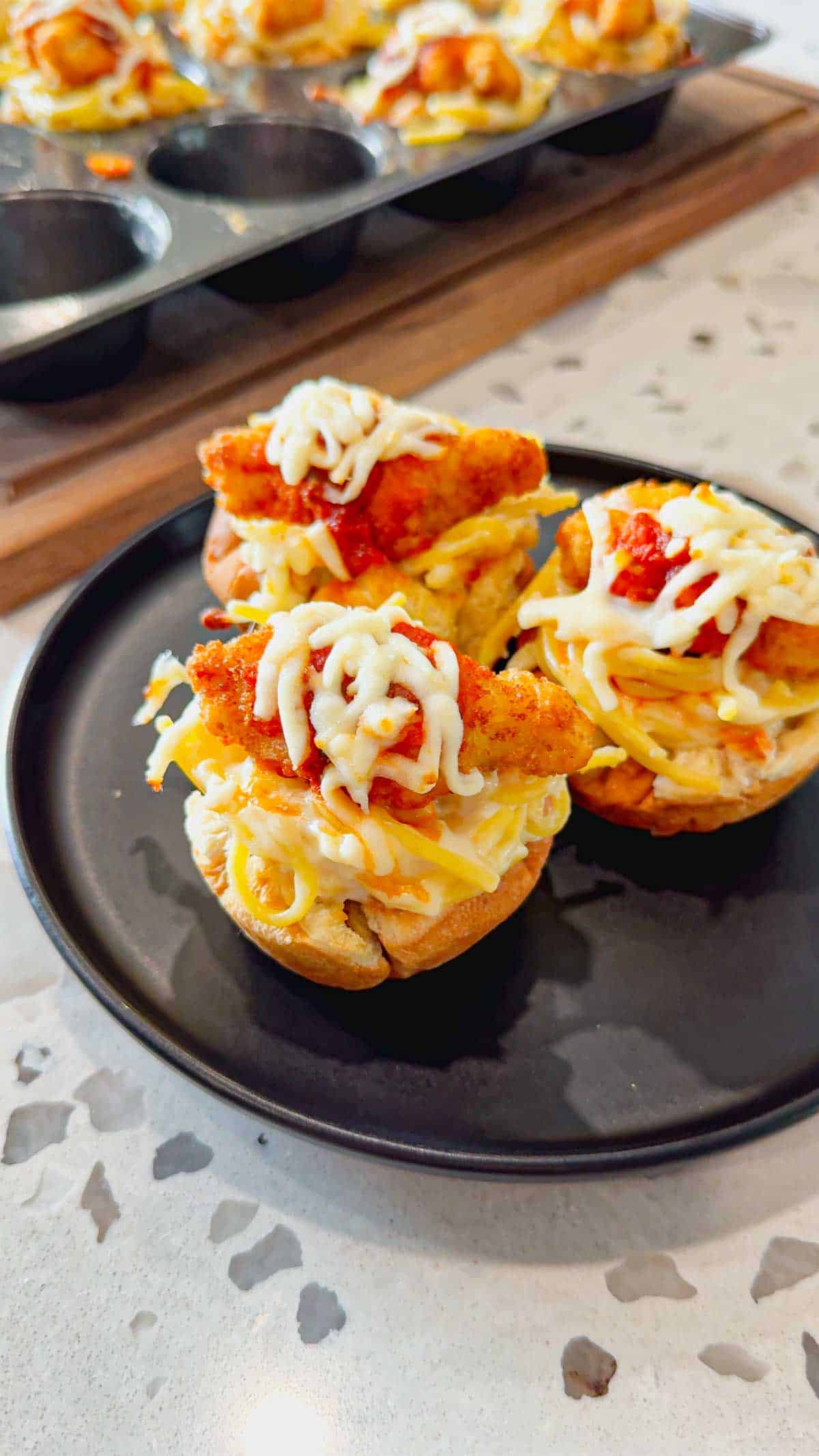 Dino Nugget Chicken Parm Cups are a fun and easy muffin tin dinner the whole family will love. Hamburger buns are spread with garlic butter, baked in muffin tins and stuffed with creamy alfredo spaghetti and topped with dino nuggets, marinara and mozzarella.