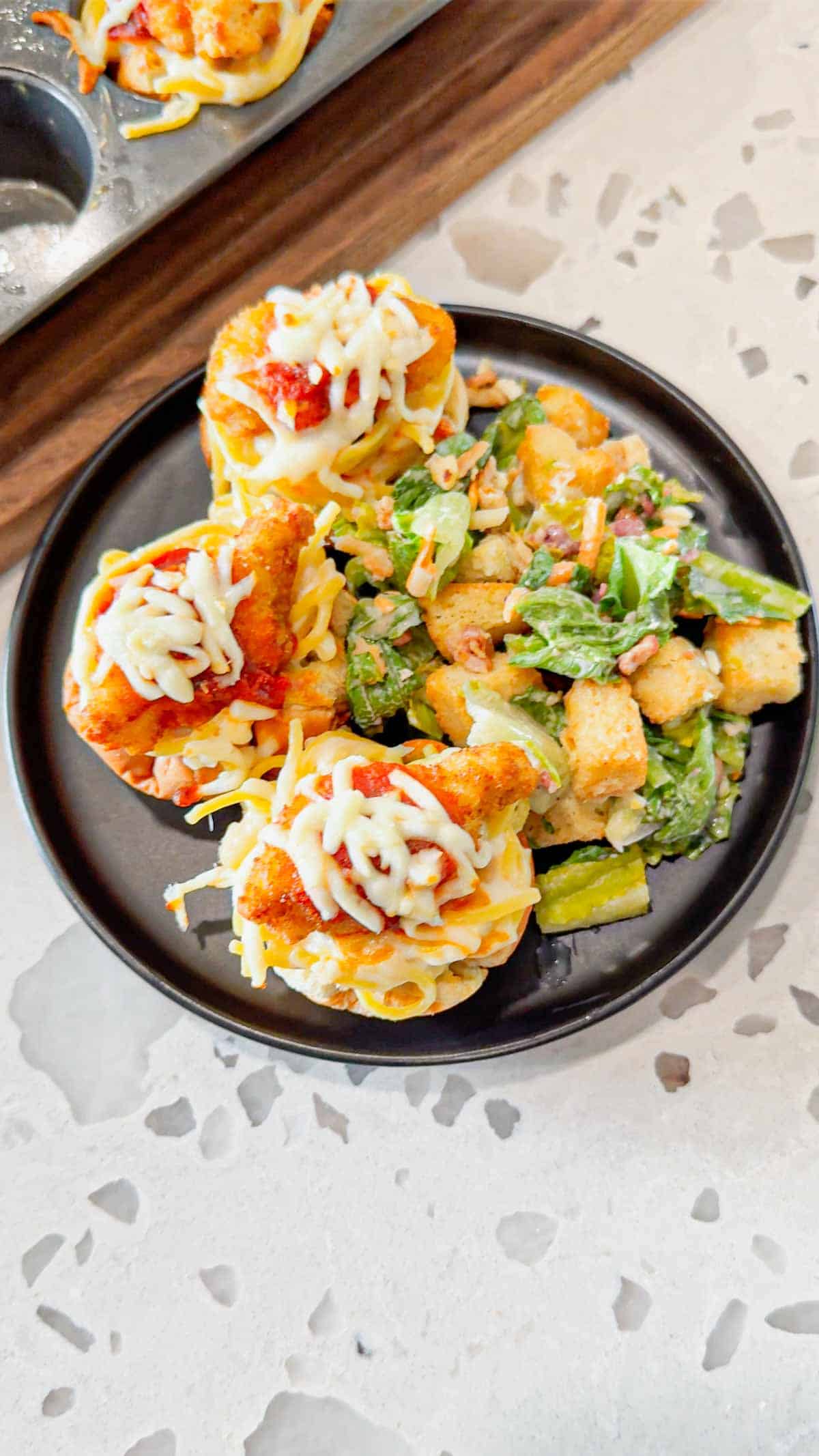 Dino Nugget Chicken Parm Cups are a fun and easy muffin tin dinner the whole family will love. Hamburger buns are spread with garlic butter, baked in muffin tins and stuffed with creamy alfredo spaghetti and topped with dino nuggets, marinara and mozzarella.
