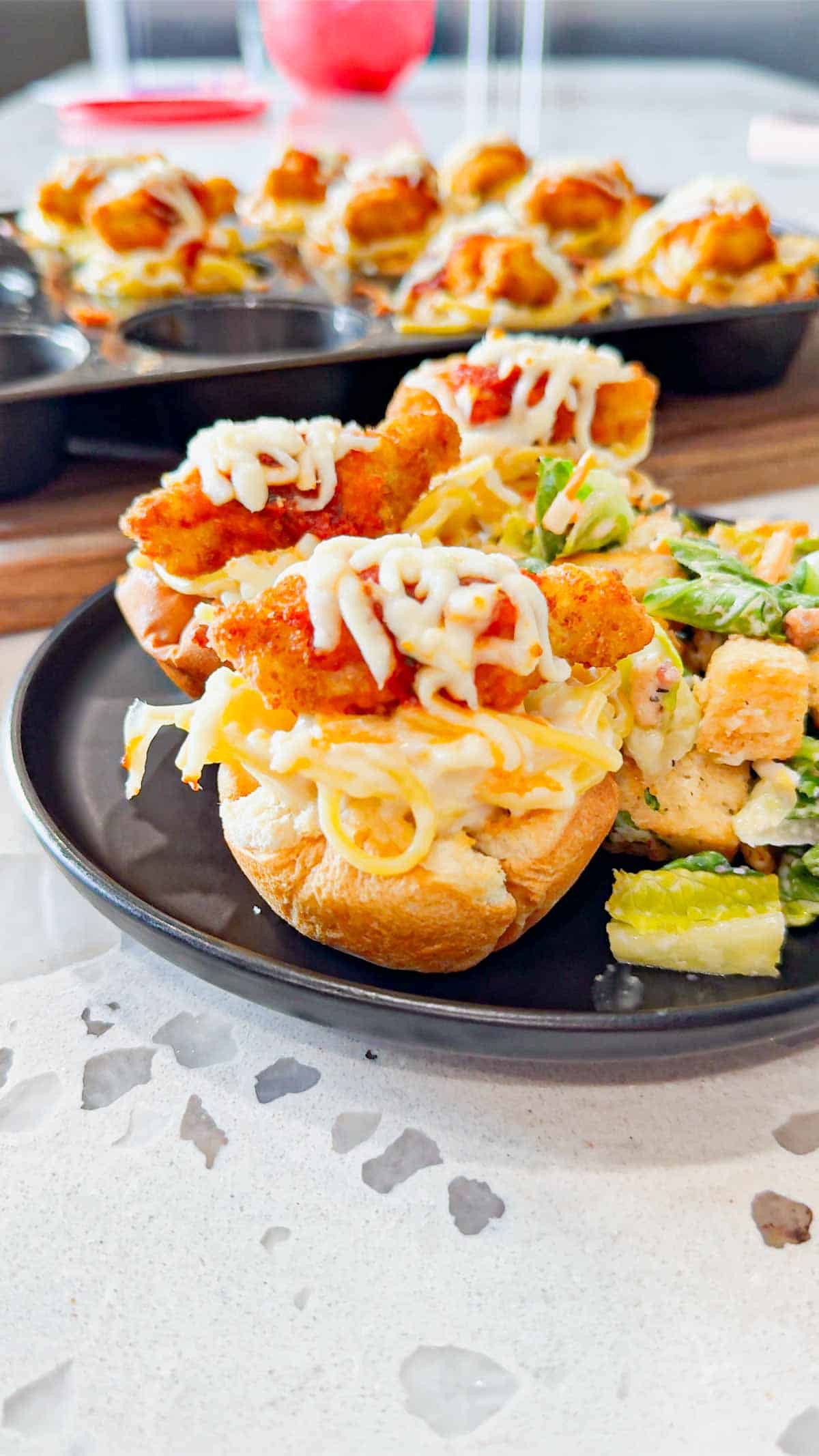 Dino Nugget Chicken Parm Cups are a fun and easy muffin tin dinner the whole family will love. Hamburger buns are spread with garlic butter, baked in muffin tins and stuffed with creamy alfredo spaghetti and topped with dino nuggets, marinara and mozzarella.