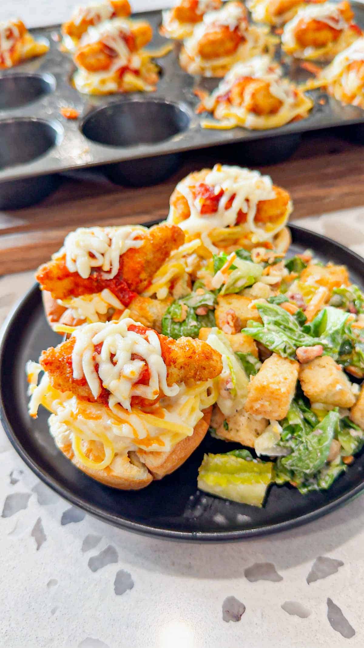 Dino Nugget Chicken Parm Cups are a fun and easy muffin tin dinner the whole family will love. Hamburger buns are spread with garlic butter, baked in muffin tins and stuffed with creamy alfredo spaghetti and topped with dino nuggets, marinara and mozzarella.