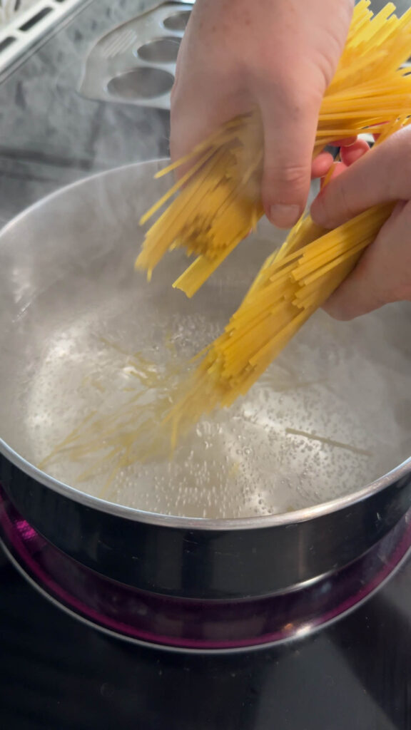 adding uncooked spaghetti noodles to a pot of boiling water