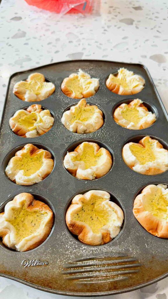 hamburger buns spread with garlic butter and stuffed into a muffin tin