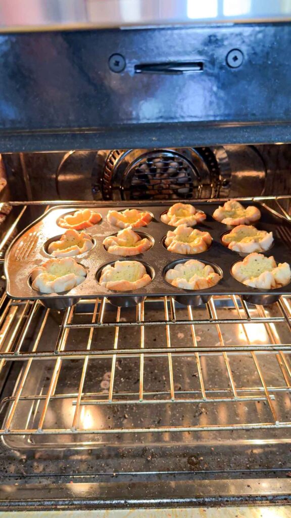 muffin tin stuffed with garlic buttered hamburger buns baking in the oven