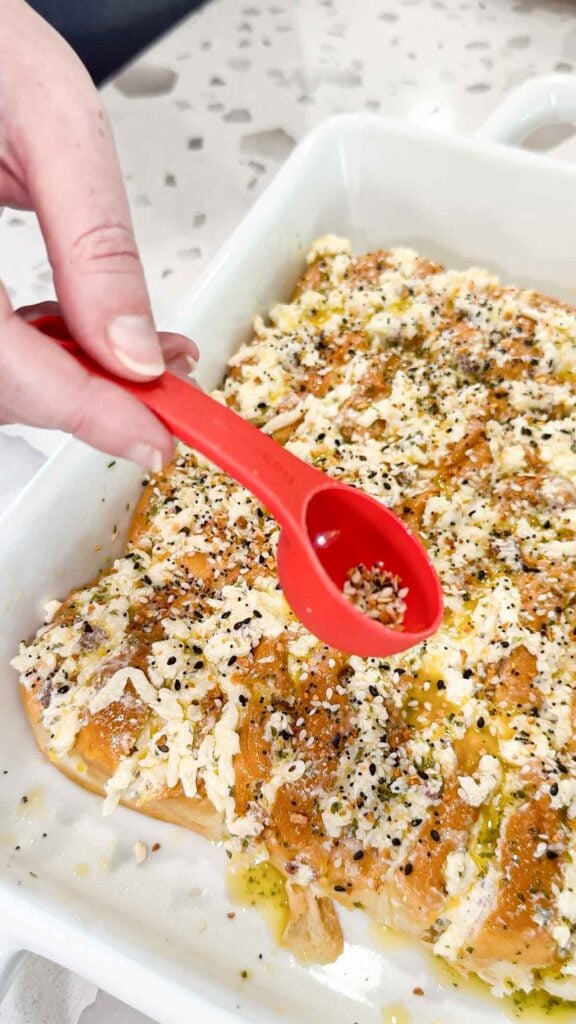 everything bagel seasoning being sprinkled on top of cheesy pull apart bread