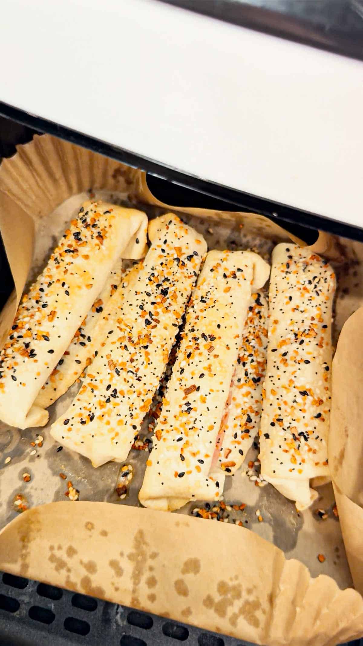 ham and cheese tortilla roll ups being pulled out of the air fryer