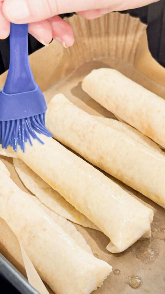butter brushed on tortilla roll ups in an air fryer basket