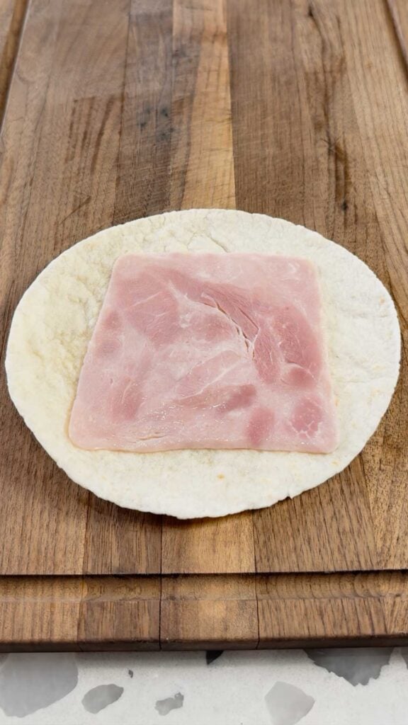a slice of ham on a flour tortilla on a cutting board
