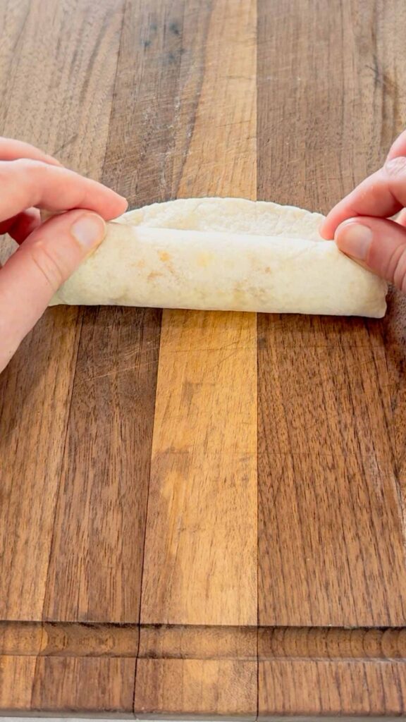 rolling up a tortilla filled with ham and a string cheese stick