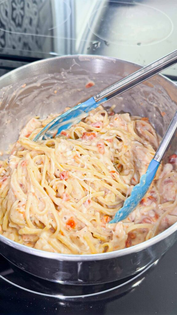 stirring grilled chicken and mozzarella cheese into linguine alfredo