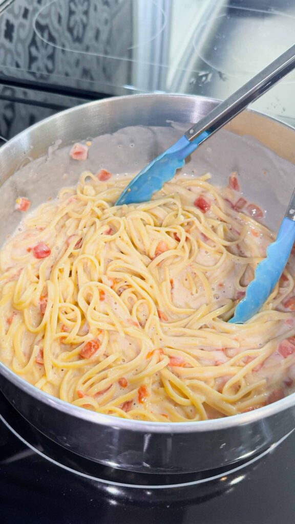 linguine alfredo with rotel diced tomatoes being stirred in a pot
