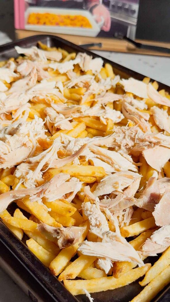 shredded turkey on top of French fries on a baking sheet