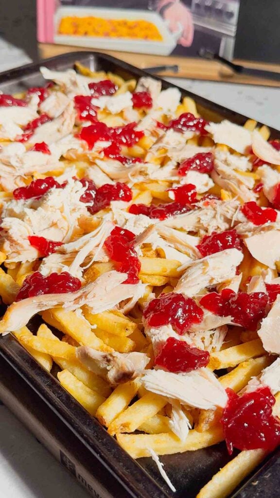 cranberry sauce spooned over shredded turkey and french fries on a baking sheet