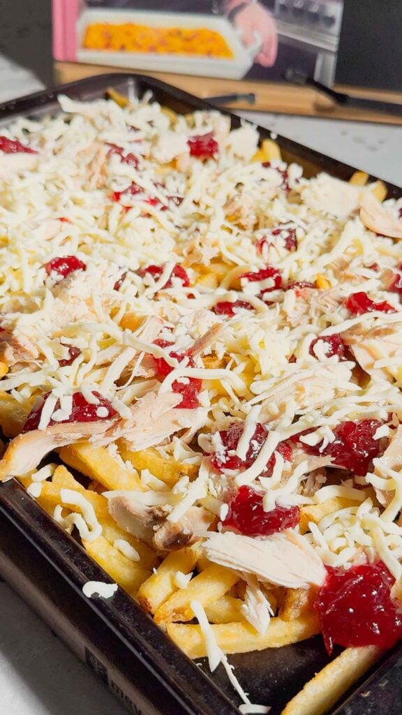 shredded mozzarella cheese on top of cranberry sauce, turkey and french fries on a baking sheet