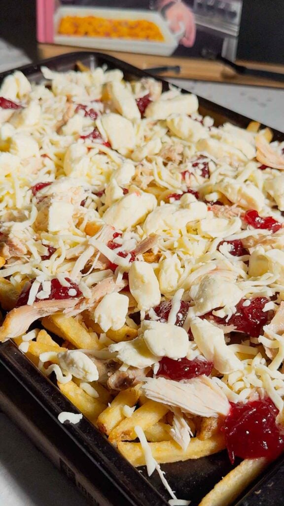 cheese curds and shredded mozzarella on top of cranberry sauce, turkey and french fries