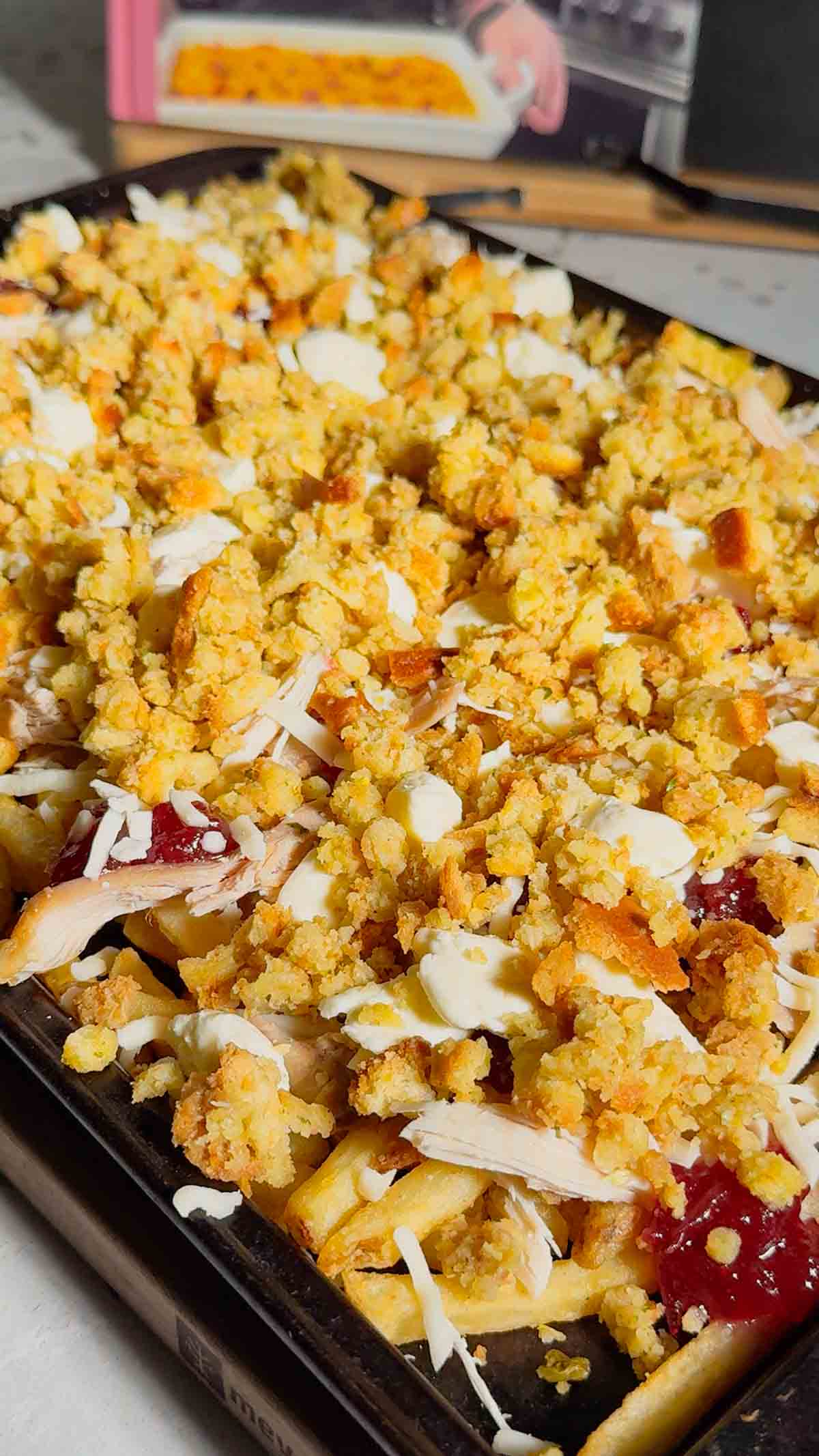stuffing, cheese, cranberry sauce and shredded turkey on top of french fries on a baking sheet