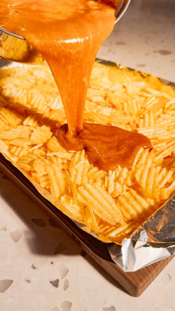 toffee being poured over ruffled potato chips on a baking sheet