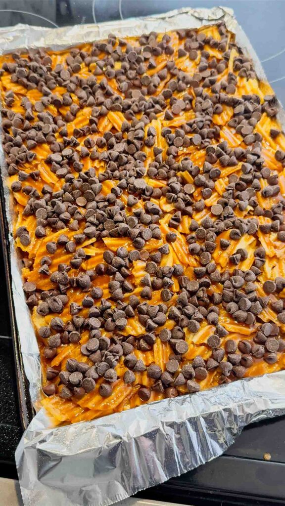semi sweet chocolate chips sprinkled over toffee coated potato chips on a baking sheet