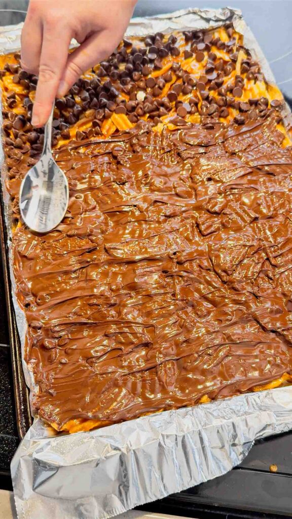 using a spoon to spread melted chocolate on top of Christmas crack