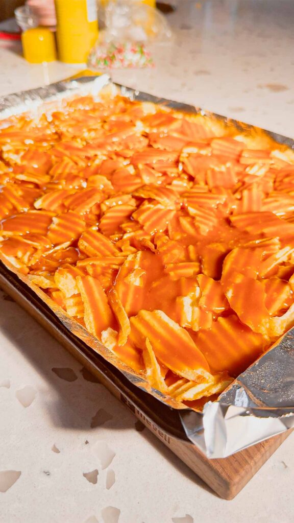toffee poured all over ruffled potato chips on a foil lined baking sheet